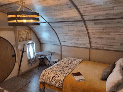 Cozy interior of a small room featuring a bed, table, and unique curved ceiling design. Warm colors and natural light.